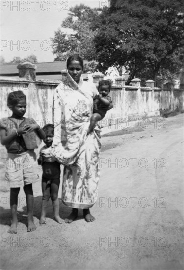 Indian woman with children. An Indian woman dressed in a sari stands, baby on hip, beside two children on a roadside verge. India, circa 1954. India, Southern Asia, Asia.
