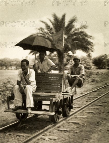 Railway hand cart. Three men sit aboard a small railway cart fitted with a wooden seat, an unusual vehicle reminiscent of a railway hand car. One of the men appears deep in contemplation, another holds up an umbrella. India, circa 1954. India, Southern Asia, Asia.