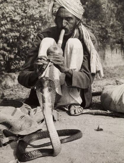 Charming a cobra. A turbaned snake charmer crouches low on the ground as he attempts to charm a cobra with a 'pungi', the musical instrument made from bamboo that is traditionally used in the art of snake charming. India, circa 1954. India, Southern Asia, Asia.