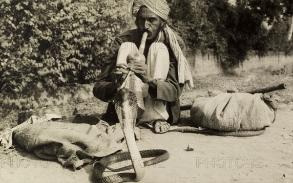 Snake charmer. A turbaned snake charmer crouches low on the ground as he attempts to charm a cobra with a 'pungi', the musical instrument made from bamboo that is traditionally used in the art of snake charming. India, circa 1954. India, Southern Asia, Asia.
