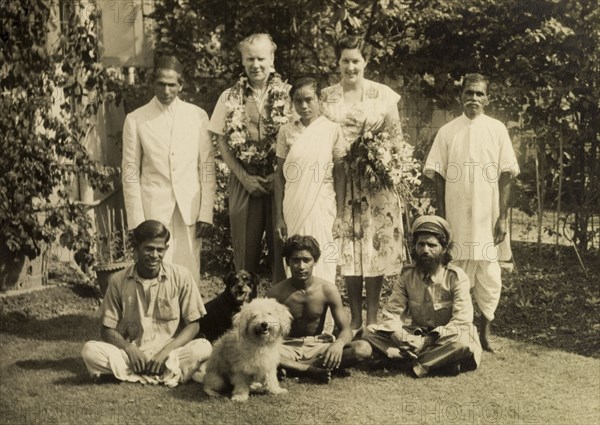 A typical a colonial household, India. Mr and Mrs Cater, adorned with flowers, pose for the camera with their team of Indian servants and two pet dogs in the garden of a colonial house. Calcutta (Kolkata), India, circa 1954. Kolkata, West Bengal, India, Southern Asia, Asia.