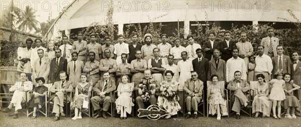 Staff at Telcalemit Ltd., Calcutta. Group portrait of the mixed race staff of Tecalemit Ltd. (TEC), taken on the occasion of the Managing Director's retirement. The more senior, mainly British employees are accompanied by their wives, including the retring MD who sits in the centre adorned with flowers. Calcutta (Kolkata), India, circa 1954. Kolkata, West Bengal, India, Southern Asia, Asia.