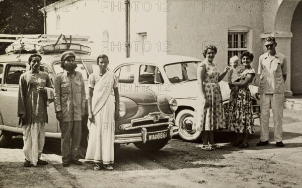 The Leonards' friends and servants. Members of the Leonard household pose for the camera as they prepare for a journey beside two cars parked in a driveway. The three Indian servants on the left are labelled in an original caption as (left to right): 'Cleaner, Driver, Ayah'. Calcutta (Kolkata), India, circa 1954. Kolkata, West Bengal, India, Southern Asia, Asia.