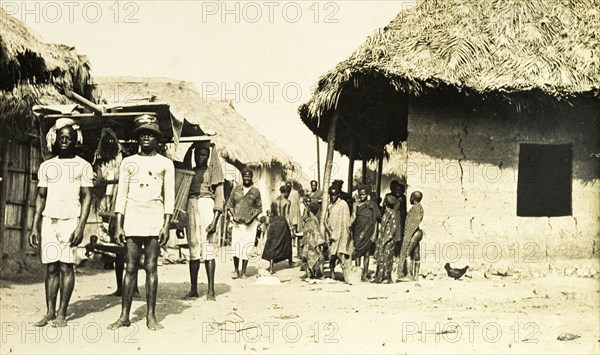 Gold Coast street scene. A group of men carry a sedan chair along a village street. Gold Coast (Ghana), circa 1920. Ghana, Western Africa, Africa.