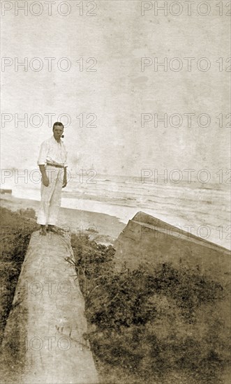 Mr Tamlin on a log. Mr Alfred Tamlin stands on a fallen log on a cliff overlooking the coast. Possibly Ghana, circa 1918., Western Africa, Africa.