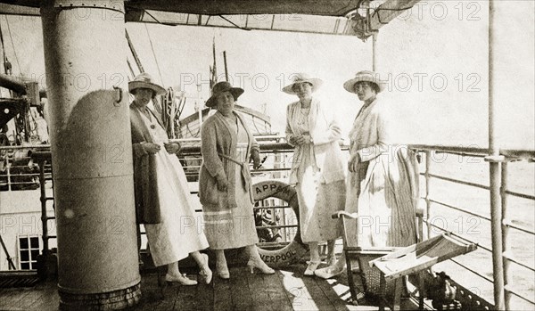 Onboard the 'Appam'. Four European women stand together on the deck of the 'Appam', a cargo and passenger ship sailing from Liverpool. They are en route to join their husbands overseas. Location unknown, circa 1918.