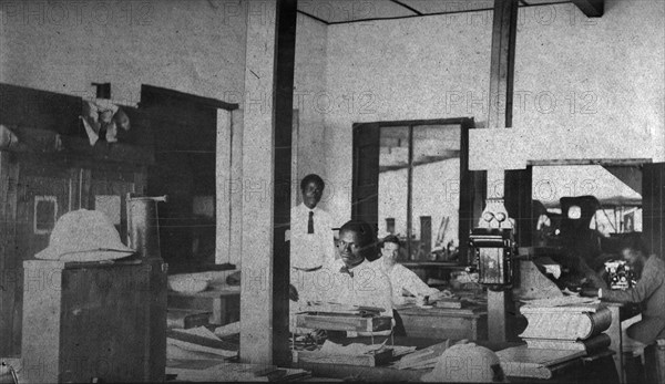 Tamlin in the office. Mr Alfred Tamlin sits in his office accompanied by three African employees. Western Africa, circa 1920., Western Africa, Africa.