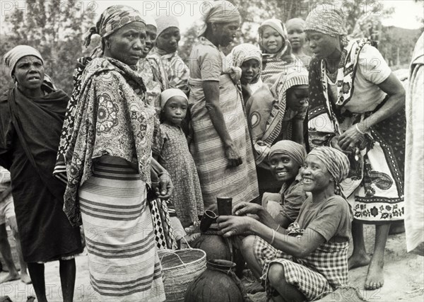 Women at a Tanganyikan market. Women laugh and chat as they examine goods at a local market. Tanganyika Territory (Tanzania), circa 1960. Tanzania, Eastern Africa, Africa.