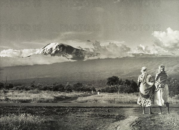 Kilimanjaro skyline. Two African women take in a view of Mount Kilimanjaro. Tanganyika Territory (Tanzania), circa 1960. Tanzania, Eastern Africa, Africa.