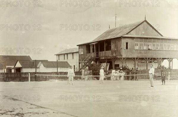 Mr. Tamlin plays tennis. Mr Alfred Tamlin (the European figure on the right) plays tennis with his colleagues. A group of Africans watch the game from the side of the court. Probably Accra, Gold Coast (Ghana), circa 1918. Ghana, Western Africa, Africa.