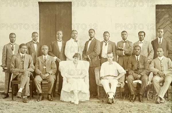 Alfred Tamlin and Miller Brothers staff. Formal group portrait of Alfred Tamlin and his wife Dorothy and the office staff of the Miller Brothers agency. The Tamlins are joined by 13 African men dressed in Western-style suits and ties. Half Assini, Gold Coast (Ghana), May 1920. Half Assini, West (Ghana), Ghana, Western Africa, Africa.