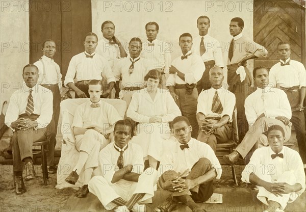Alfred Tamlin and Miller Brothers staff. Group portrait of Alfred Tamlin and his wife Dorothy (nee Lamble) and the local staff of the Miller Brothers agency. The Tamlins are joined by 15 African men dressed in Western-style trousers, shirts and ties, but no jackets. Half Assini, Gold Coast (Ghana), May 1920. Half Assini, West (Ghana), Ghana, Western Africa, Africa.
