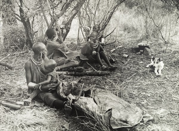Maasai family group. Official publicity shot for the Tanganyikan government. Maasai women and children sit on the ground at a temporary camp site. Tanganyika Territory (Tanzania), circa 1960. Tanzania, Eastern Africa, Africa.