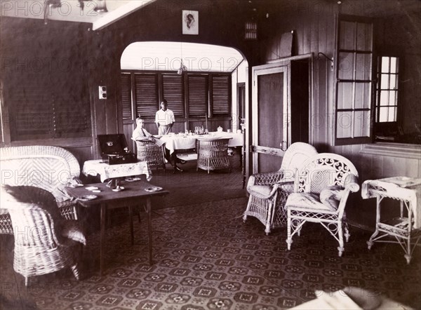 Interior of Swanzy's managers' bungalow. Alfred Tamlin and a domestic servant photographed in the dining room of the managers' bungalow of the Motor Transport Depot of F & A Swanzy Limited. Accra, Gold Coast (Ghana), 4 April 1918. Accra, East (Ghana), Ghana, Western Africa, Africa.