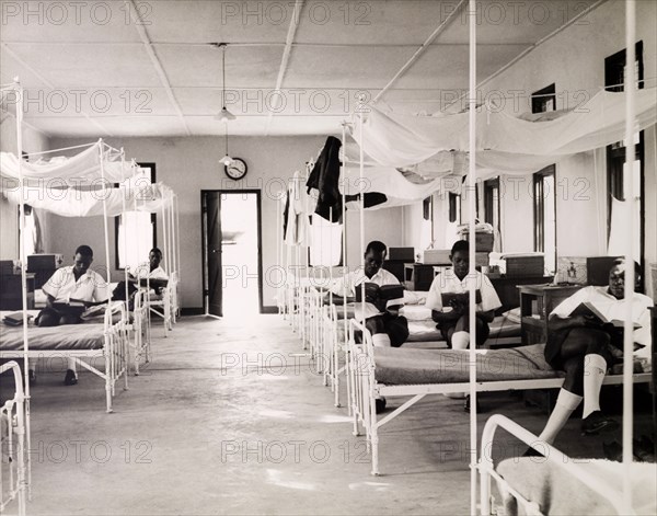 Dormitory at a Tanganyikan college. Official publicity shot for the Tanganyikan government. A group of young men in uniform read quietly on their bunks in a college dormitory. Tanganyika Territory (Tanzania), circa 1950. Tanzania, Eastern Africa, Africa.