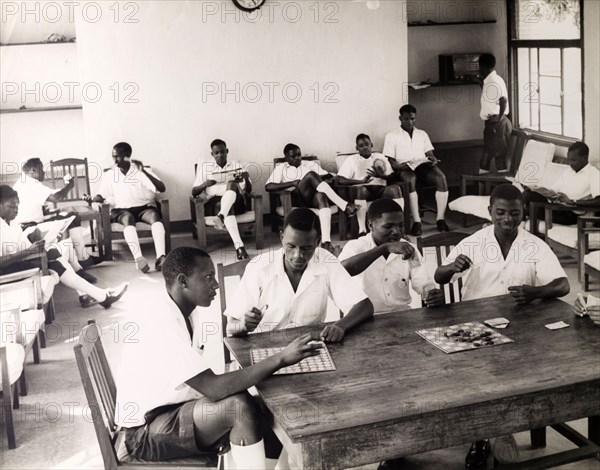 Recreation at a Tanganyikan college. Official publicity shot for the Tanganyikan government. A group of young men in uniform play cards and draughts whilst others read during a college recreation period. Tanganyika Territory (Tanzania), circa 1950. Tanzania, Eastern Africa, Africa.