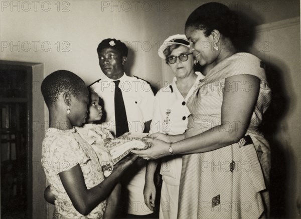 Staff meet patients at a British Red Cross Clinic. Staff meet patients at a Children's Welfare Clinic run by the British Red Cross, during a royal visit from Princess Mary, Countess of Harewood. The staff are identified left to right as: Mr F.O. Sholeye (Regional Secretary), Mrs E.C. Alderton (Regional Nursing Superintendant) and Mrs Mhamdi Azikiwe (Regional Director). Enugu, Anambra State, Nigeria, 16 November 1957., Enugu, Nigeria, Western Africa, Africa.