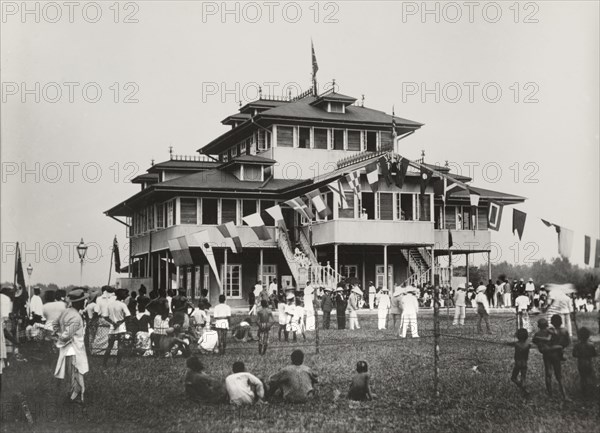Sports activities outside the Vice Consulate. A group of European men play a team game, possible cricket, in front of the Vice Consulate in Bonny. A crowd of predominantly Nigerian spectators watch from the sidelines. Bonny, Rivers State, Nigeria, 1900. Bonny, Rivers, Nigeria, Western Africa, Africa.