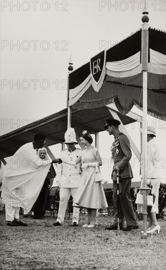 Queen Elizabeth II meets Dr Nnamdi Azikiwe. Dr Nnamdi Azikiwe, Premier of Eastern Nigeria, shakes hands with Queen Elizabeth II at an official reception during her royal tour of the country (28 January-16 February 1956). To her left stands Prince Philip, Duke of Edinburgh, and to her right, a uniformed dignitary, probably the Governor General of Nigeria, Sir James Robertson. Nigeria, circa January 1956. Nigeria, Western Africa, Africa.