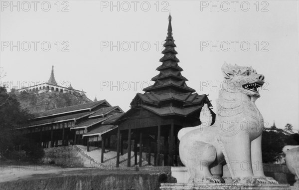 Sphinx statue at the Shwe Dagon Pagoda. A sphinx statue stands guard over a large wooden pagoda with a tiered roof, in front of a covered flight of steps, which lead up to a hilltop pagoda in the distance. Rangoon (Yangon), Burma (Myanmar), circa 1925. Yangon, Yangon, Burma (Myanmar), South East Asia, Asia.