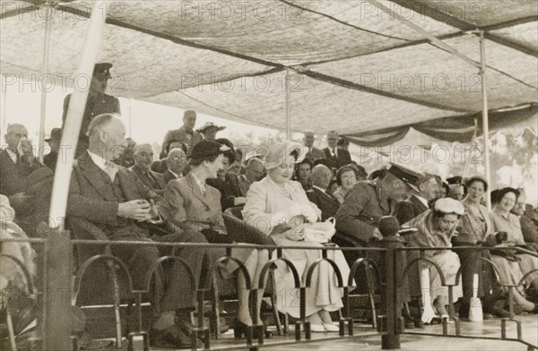 The Queen Mother and Princess Margaret in Rhodesia, 1953. Queen Elizabeth, The Queen Mother (centre), and her daughter Princess Margaret (right, bending down), sit beneath a canopy at an outdoor event during a royal visit to Southern Rhodesia. Southern Rhodesia (Zimbabwe), July 1953. Zimbabwe, Southern Africa, Africa.