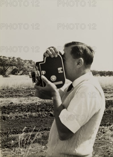 Filming for the Central African Film Unit. A European cameraman operates a movie camera during a film shoot for the Central African Film Unit (CAFU). Probably Southern Rhodesia (Zimbabwe), circa 1955. Zimbabwe, Southern Africa, Africa.
