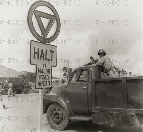 An armed African soldier on the back of truck. An African soldier stands on the back of a stationary truck, resting his gun on the roof of the cab. This photograph was taken during a film shoot for the Central African Film Unit (CAFU) and may feature an actor on set. Probably Southern Rhodesia (Zimbabwe), circa 1955. Zimbabwe, Southern Africa, Africa.