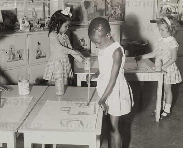 A mixed race class. A Northern Rhodesian Information Department photograph shows three young schoolgirls (one African, one Asian and one European) painting together in class. Northern Rhodesia (Zambia), circa 1950. Zambia, Southern Africa, Africa.