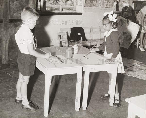 Frederick Knapp School. A Northern Rhodesian Information Department photograph shows two young schoolchildren, a European boy and an Asian girl, painting together in class at the Frederick Knapp School. Northern Rhodesia (Zambia), circa 1950. Zambia, Southern Africa, Africa.