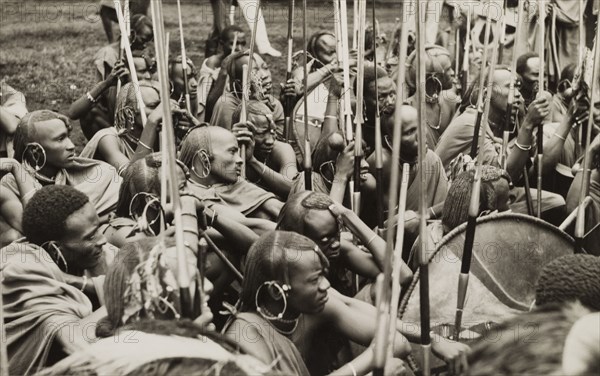 A group of Maasai warriors. A group of Maasai warriors crouch together on the ground with their upright spears, displaying traditional hairstyles and jewellery. Eastern Africa, circa 1955., Eastern Africa, Africa.