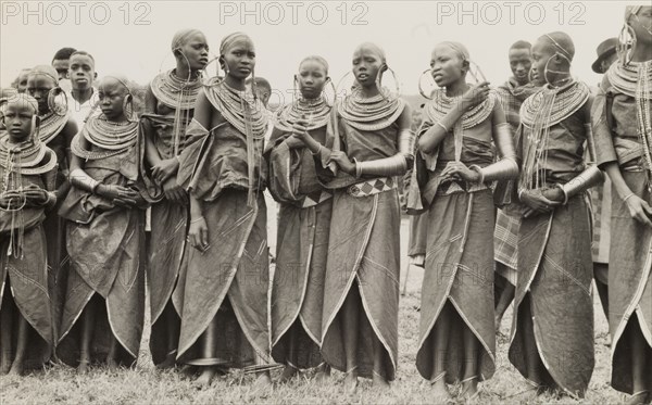 A group of Maasai women. A traditionally dressed group of young Maasai women stand in line. Their heads are shaven and they wear ornate jewellery including large hooped earrings, armlets and masses of beaded necklaces. Eastern Africa, circa 1955., Eastern Africa, Africa.