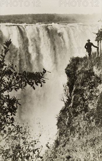 Overlooking Victoria Falls. A man stands on the edge of a cliff overlooking Victoria Falls, a spectacle known locally as 'Mosi-oa-Tunya' or the 'smoke that thunders'. Matabeleland, Southern Rhodesia (Matabeleland North, Zimbabwe), circa 1950., Matabeleland North, Zimbabwe, Southern Africa, Africa.