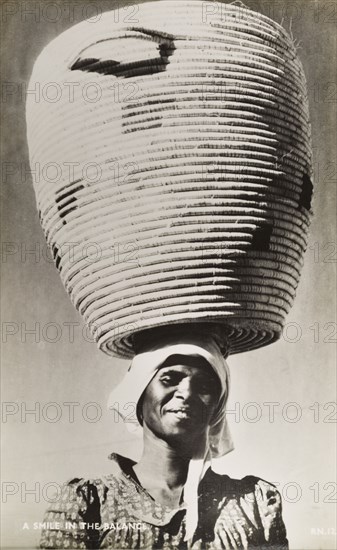 A smile in the balance'. A smiling woman balances a huge basket on her head. Southern Africa, circa 1950., Southern Africa, Africa.