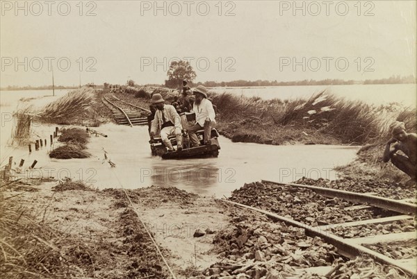 Without a paddle. Three men attempt to cross a flooded section of railway line on a small, hand-operated cart. Built on a raised embankment, the track is partially submerged by the waters of a swollen river. West Bengal, India, circa 1920., West Bengal, India, Southern Asia, Asia.