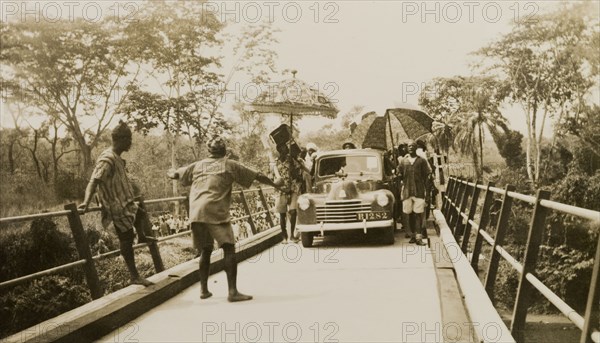 Opening of the Ishua to Ibillo bridge. People with parasols surround the first car to cross the Ishua to Ibillo road bridge at its official opening. Ondo, Nigeria, 5 January 1951., Ondo, Nigeria, Western Africa, Africa.