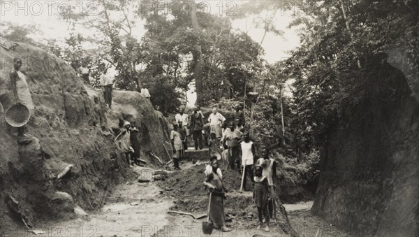 Widening the road from Imesi-Ile. A local labour force of men, women and children work to widen the road leading from Imesi-Ile. A European land owner identified as 'Kendal Robinson, the Resident', stands amongst the group. Osun, Nigeria, circa 1950., Osun, Nigeria, Western Africa, Africa.