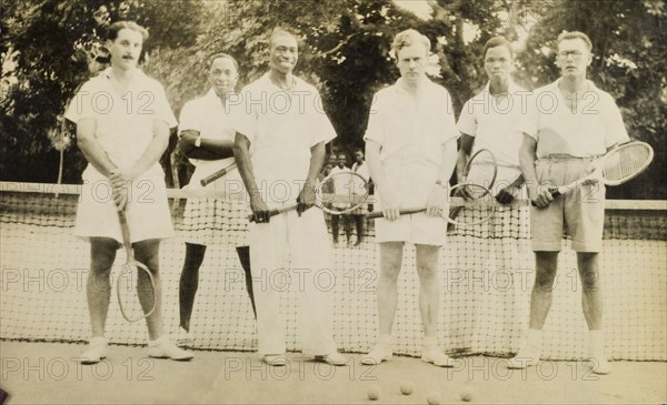 Mixed trebles. Six British and Nigerian men pose for the camera holding tennis racquets during a break in their game. They are identified as (left to right): Cyril Iles (colonial officer), Olafinha (trader), Olowo, Joslin (Assistant District Officer), Oshopora (Treasury Clerk), Duggie White (Inspector of Works). Probably Ondo, Nigeria, March 1950., Ondo, Nigeria, Western Africa, Africa.