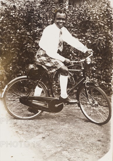 A Nigerian man in tartan. Portrait of a Nigerian man on a bicycle, dressed in a tartan kilt and tie, a white shirt and long socks. Ondo, Nigeria, circa 1949., Ondo, Nigeria, Western Africa, Africa.