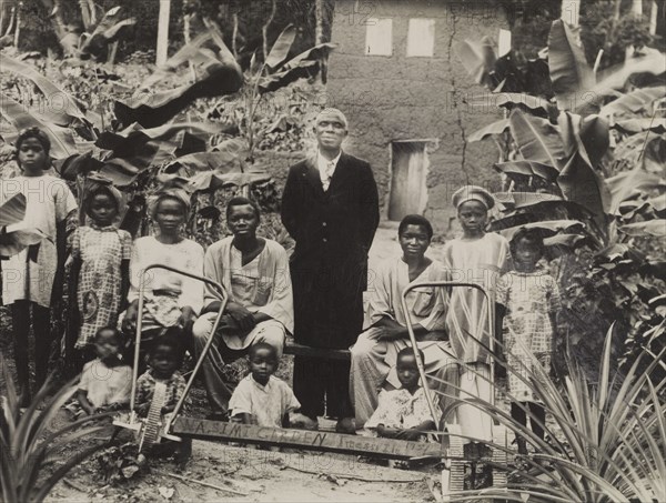 Children in 'Wasimi Garden'. Children gather around an adult male for a group photograph in 'Wasimi Garden', the name indicated by a handmade sign. Two hand-operated tilling machines sit in the foreground. Imesi-Ile, Nigeria, 1951. Imesi-Ile, Osun, Nigeria, Western Africa, Africa.