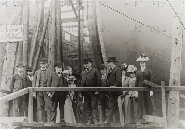 Sir Alfred Holt at a dockyard. A group of formally dressed men and women pose for the camera beside the bow of a large ship in dry dock. Amongst the group is Sir Alfred Holt (fourth from right), founder of the Blue Funnel shipping line. United Kingdom, circa 1890. England (United Kingdom), Western Europe, Europe .