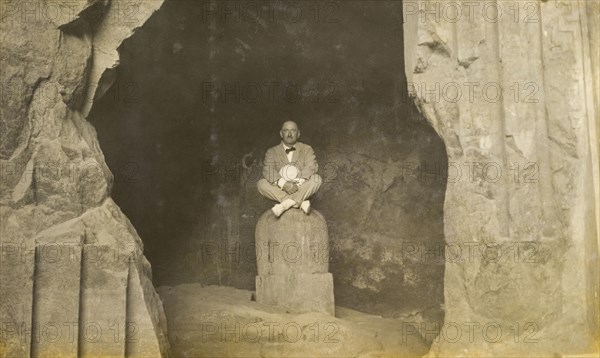 Inside the Elephanta Caves. A European man sits cross-legged, posing for the camera on a stone sculpture inside the Elephanta Caves. Elephanta Island, Maharashtra, India, circa 1920. Elephanta Island, Maharashtra, India, Southern Asia, Asia.