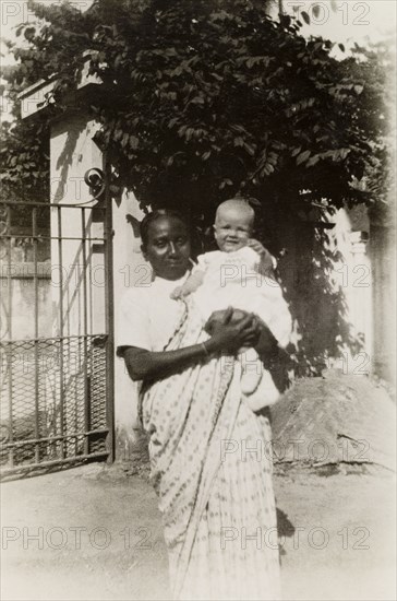 Ayah with baby. An Indian ayah (nursemaid) holds a British baby outside the gates of a colonial residence. Calcutta (Kolkata), India, 1932. Kolkata, West Bengal, India, Southern Asia, Asia.