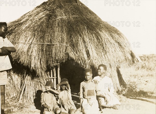 Children of African workers at Balloch Farm. Four African children, belonging to workers at Balloch Farm, pose for the camera at the entrance to a round, thatched hut. Near Gwelo, Southern Rhodesia (near Gweru, Zimbabwe), circa 1930. Gweru, Midlands, Zimbabwe, Southern Africa, Africa.