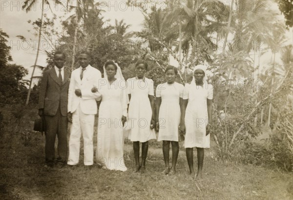 A European-style African wedding. A newlywed African couple pose outdoors with their best man and three bridesmaids: all are dressed in traditionally European-style clothing. Coast Province, Kenya, 1952., Coast, Kenya, Eastern Africa, Africa.