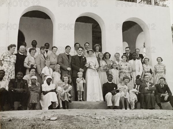Methodist missionary marriage in Kenya. English Methodist missionary, Reverend Ian Lewis, and his new wife, Audrey (nee Colman), pose beneath the arches of the manse (minister's house) at Mazeras for a wedding portrait with their family and friends. Mazeras, Kenya, 6 September 1952. Mazeras, Coast, Kenya, Eastern Africa, Africa.