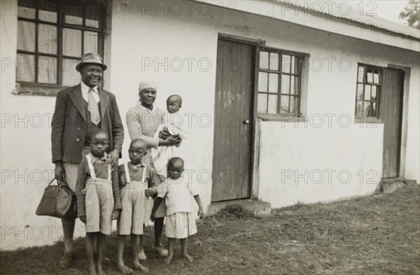 A theology student and his family, Kenya. A student of St. Paul's United Theological College in Limuru, stands with his wife and four children outside a single storey house, provided for him and his family by the college. The college was established by missionaries to train African ordinands for the priesthood and to educate their wives. Limuru, Kenya, circa 1956. Limuru, Central (Kenya), Kenya, Eastern Africa, Africa.