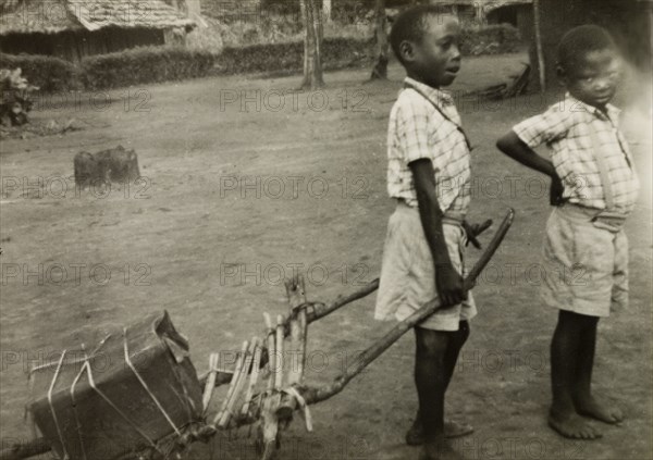 Boys at Mombasa Intermediate School. Two young boys in uniform play outside Mombasa Intermediate School. The taller boy pulls a parcel along the ground using a homemade wooden stretcher. Mombasa, Kenya, circa 1956. Mombasa, Coast, Kenya, Eastern Africa, Africa.
