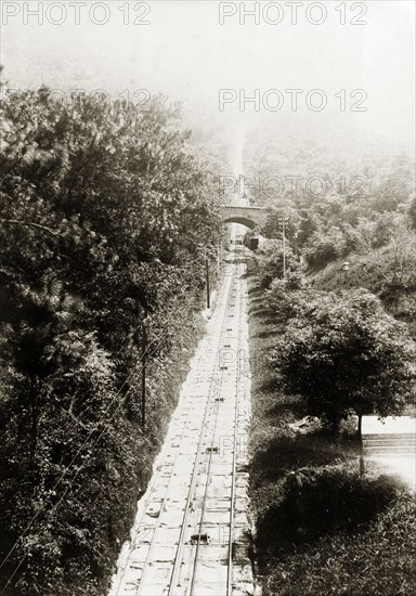 The Peak Tramway, 1903. View of the Peak Tramway, a funicular railway leading to Victoria Peak. The traction cable used to power the cars is visible in the centre of the tracks, with a small footbridge crossing the line in the distance. Hong Kong, China, 1903. Hong Kong, Hong Kong, China, People's Republic of, Eastern Asia, Asia.