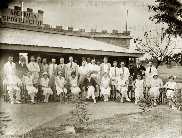Members of the Abeokuta Sports Club. A number of European men and women line up for a group portrait outside the Abeokuta Sports Club. The men stand in the back row wearing casual suits, whilst the women sit on chairs, dressed in tennis whites and holding racquets. Abeokuta, Ogun State, Nigeria, circa 1929. Abeokuta, Ogun, Nigeria, Western Africa, Africa.