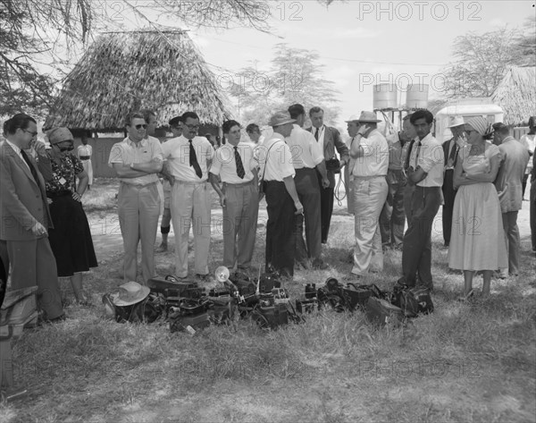 Photographers at Amboseli. Photographers at a welcoming ceremony for Princess Margaret wait for something to happen, their cameras heaped together in a pile on the ground. Amboseli, Tanganyika Territory (Tanzania), 23 October 1956. Amboseli, Kilimanjaro, Tanzania, Eastern Africa, Africa.